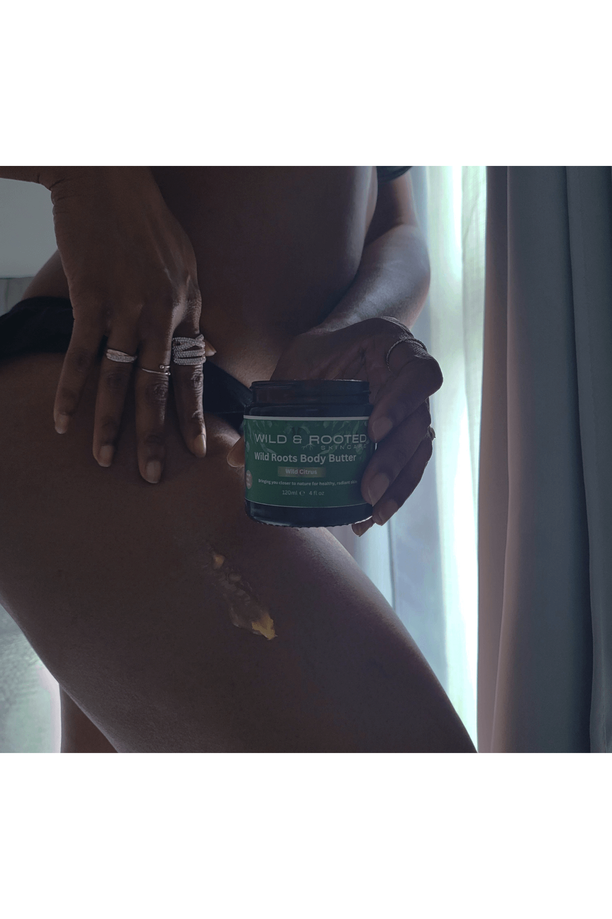 Woman standing by window holding a jar of Wild Roots Body Butter