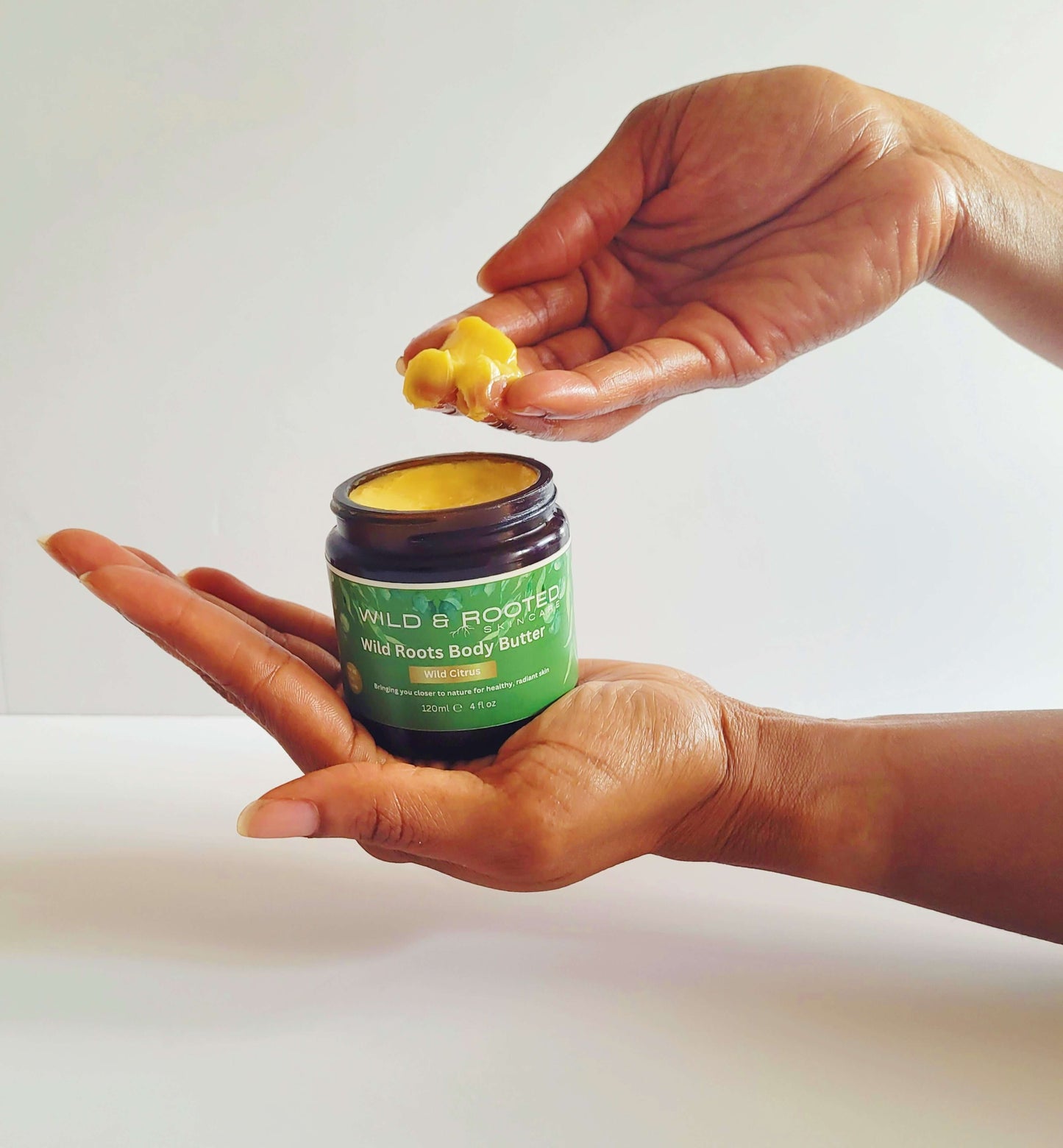 A hand scooping out body cream from a jar